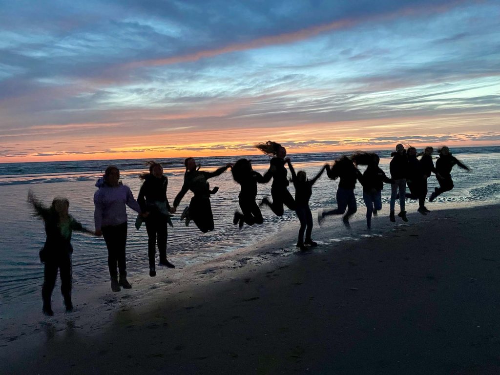 Silhouetten van Scouts die tegelijk springen in de branding tijdens zonsondergang – zomerkamp Scouting PPD